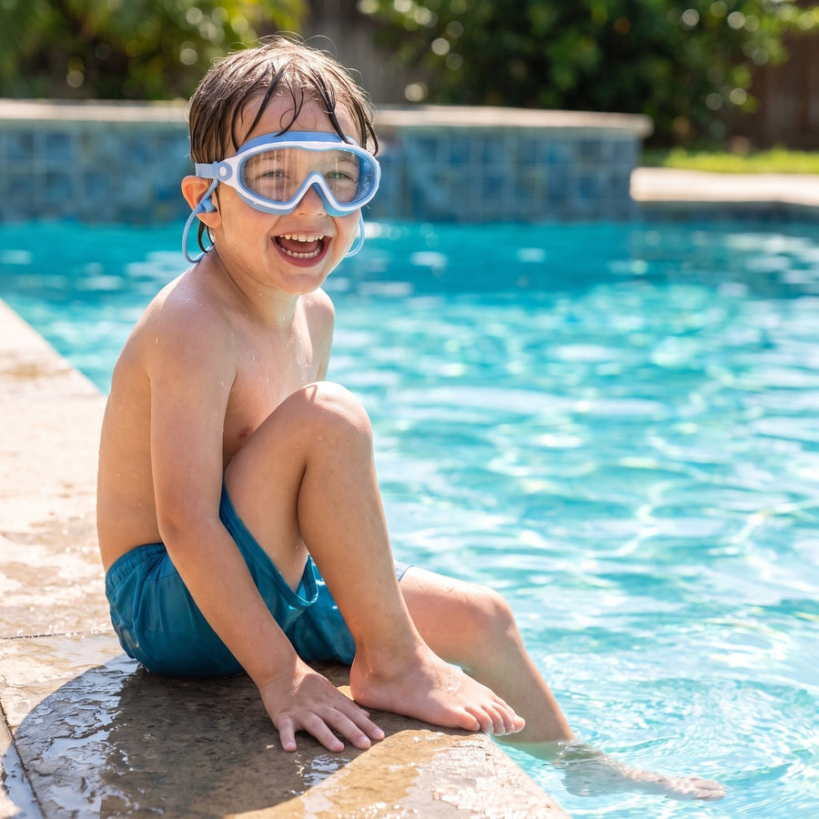 Laughing child sitting on the pool edge wearing blue Wavlee kids swim goggles