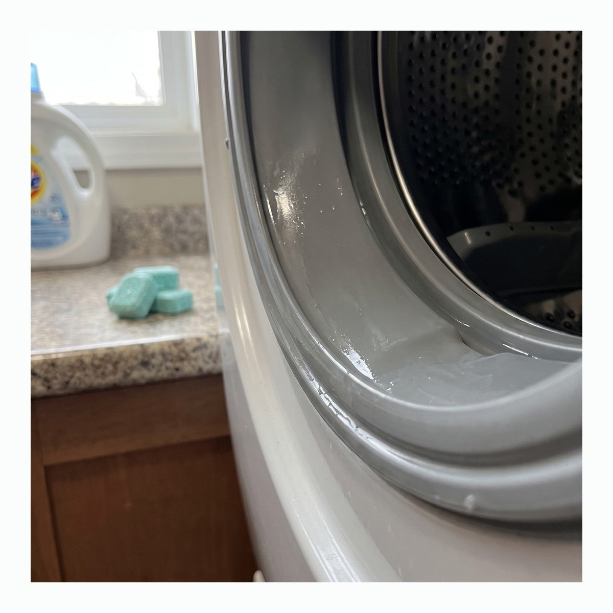 Empty front-loader drum and seal with mint washer cleaner tablets nearby